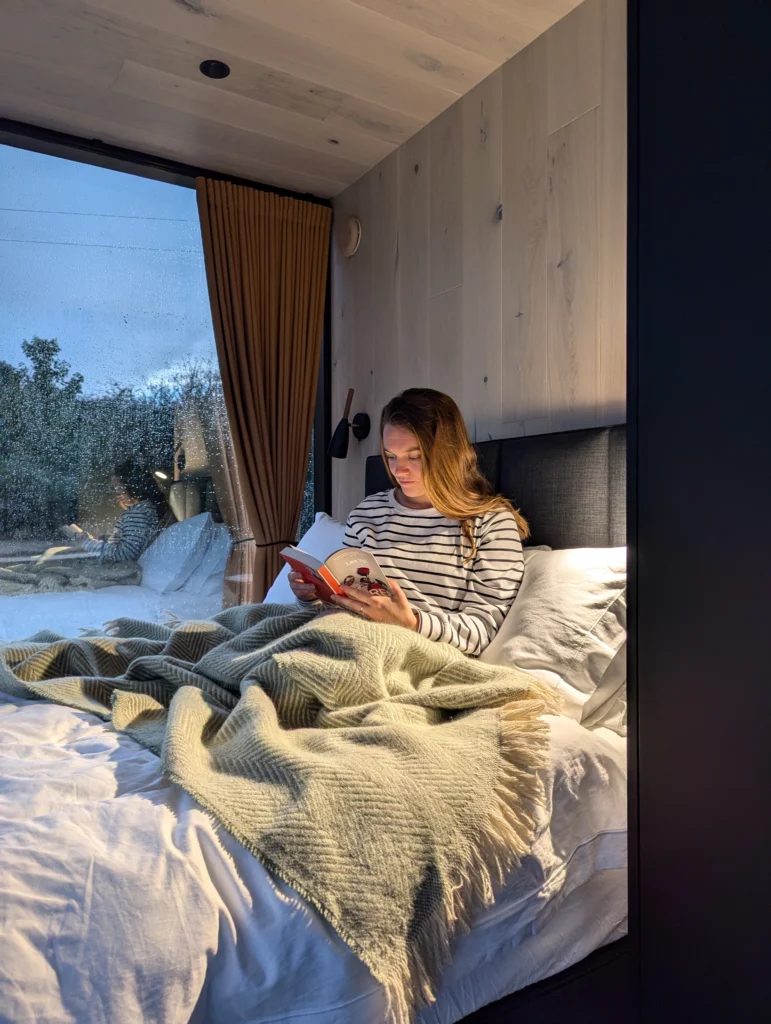 A snap of Justyn reading a book in the bed at OOD Mirror House: Meadow. 