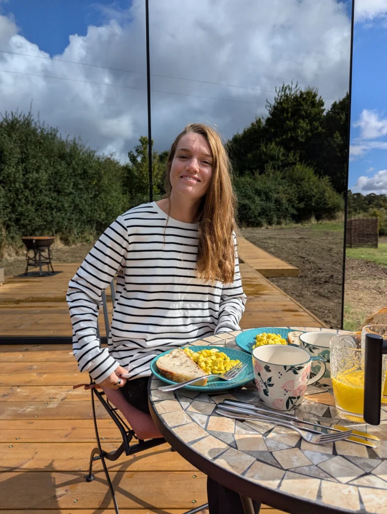 A picture of Justyn eating breakfast with Pound Farm OOD Mirror House in the background. 