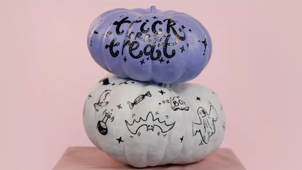 Two pumpkins (painted white and purple) stacked ontop of each other. The purple pumpkin on top reads 'Trick of Treat'