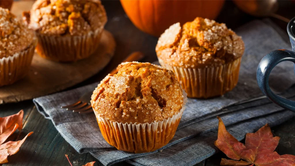 Pumpkin flavored muffins with a pumpkin in the background.