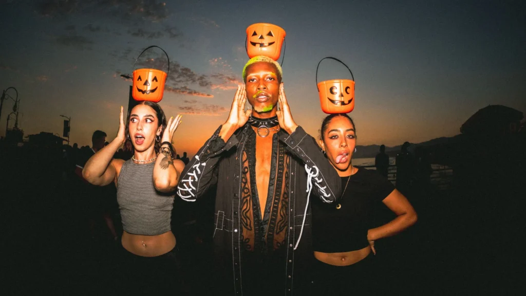 A picture of 3 people dressed chic with Halloween pumpkin candy buckets. 