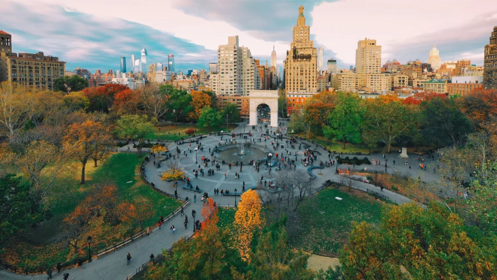 A photo of a park in the fall, with beautiful fall colors and a city in the background.